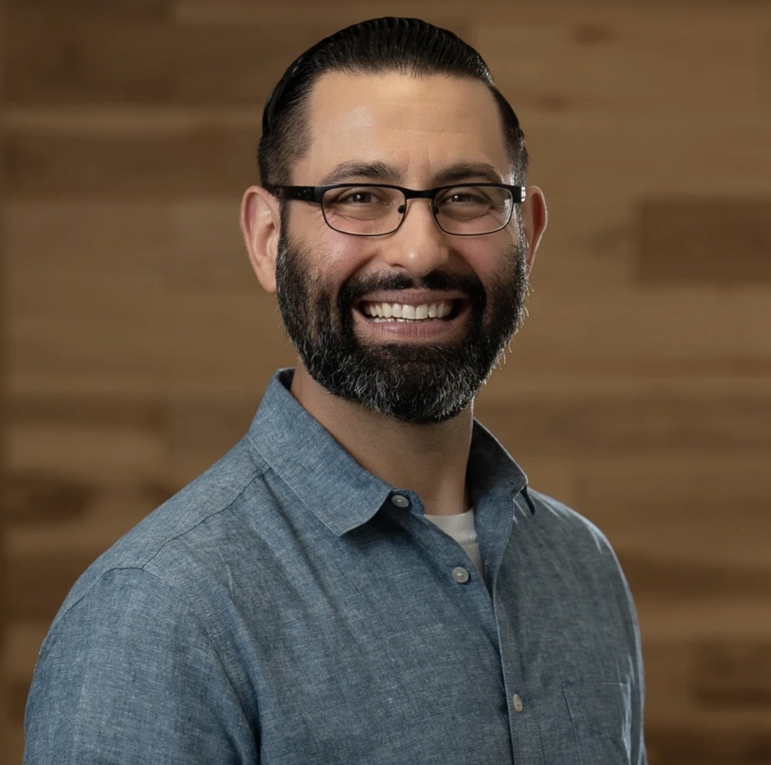 Jesse Reed smiling, wearing glasses and a blue shirt